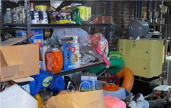Basement storage area before cleaning — shelving and floor stacked with boxes, bags and household items