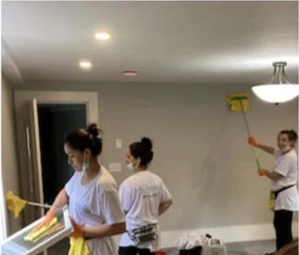 Three members of the Vcleaning team cleaning a newly finished room — a window frame, a wall and a ceiling light